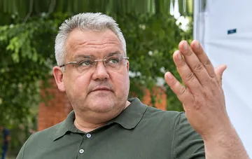 Former Belgorod mayor Polezhaev in a photo: a man in an olive polo shirt and rimless glasses raising his hand against a green backdrop