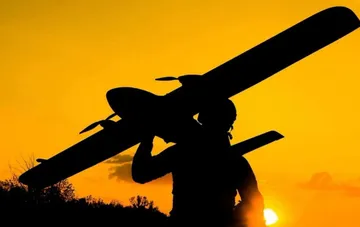 Силует оператора з дроном-камікадзе Shahed на плечах на тлі помаранчевого заходу — ілюстрація нічної масованої атаки 212 безпілотників