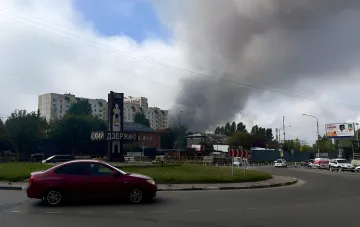 Cityscape with a 'Dzerzhinsk' sign and dark storm clouds over residential buildings — illustration for the news on the shutdown of Gazprom Neft's Moscow refinery after drone strikes