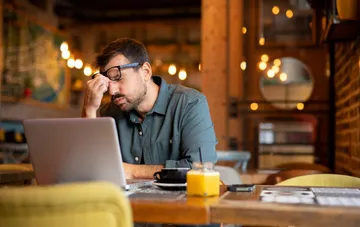 A tired sole proprietor works on a laptop in a cafe amid news of a new 85,000 euro turnover threshold for VAT