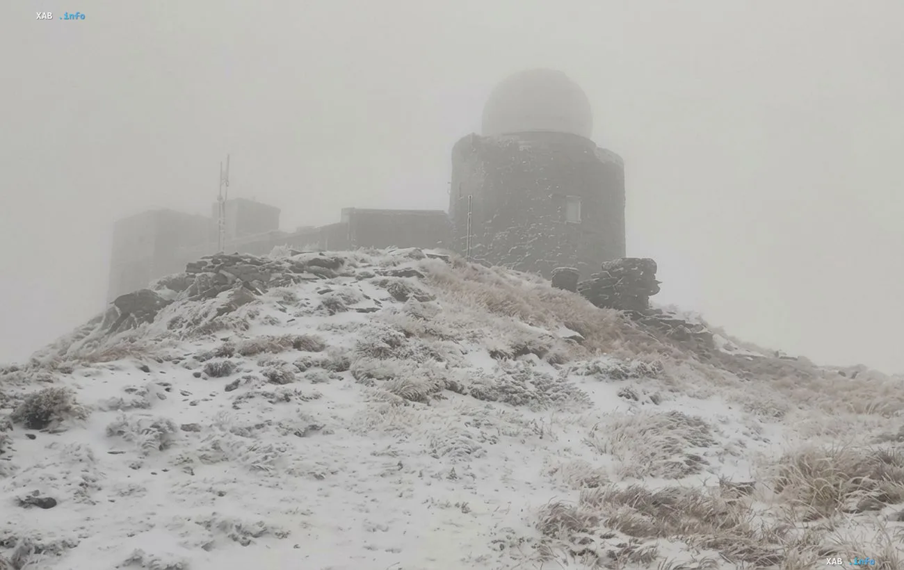 First snow of September on Pop Ivan mountain in the Carpathians: a dome-topped weather station and snow-covered slope shrouded in fog below freezing