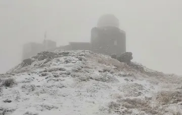 First snow of September on Pop Ivan mountain in the Carpathians: a dome-topped weather station and snow-covered slope shrouded in fog below freezing