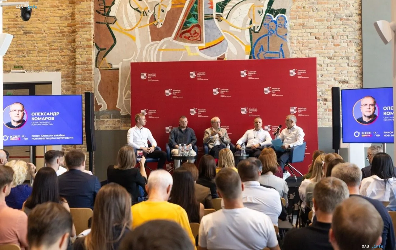 Panel discussion on the Ukrainian capital market at the KIEF TALKS conference: speakers on stage in front of an audience, with the KIEF logo and speaker Oleksandr Komarov on the screens