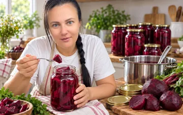 Woman tasting pickled beets from a jar with homemade winter preserves in the background
