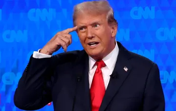 Дональд Трамп указывает пальцем на висок на фоне синего экрана с логотипами CNN во время выступления, на фоне конфликта телеканалов США и запрета доступа CNN