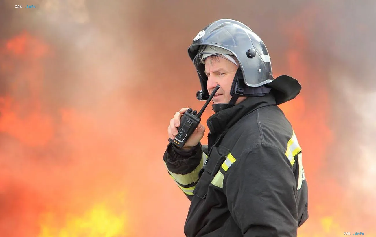 Firefighter in a protective helmet coordinates via radio against a backdrop of flames after a strike on a Russian oil refinery