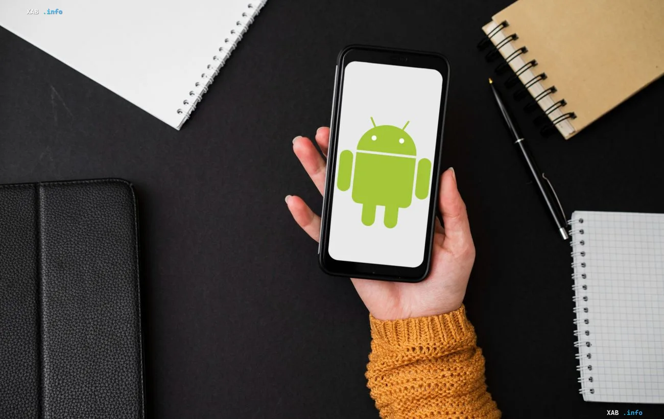 Смартфон с логотипом Android в руке на рабочем столе — символ 18-летия платформы