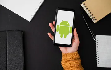 Смартфон с логотипом Android в руке на рабочем столе — символ 18-летия платформы