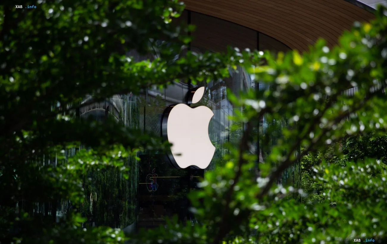 Apple logo on a store's glass facade framed by lush green foliage, in the context of the company preparing a screenless fitness tracker to rival Whoop
