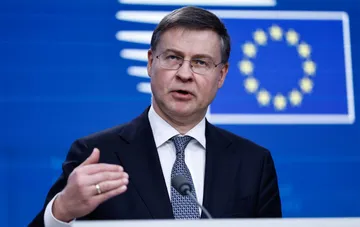 EU Commissioner speaks at a press conference against the backdrop of the EU flag, calling for stronger sanctions pressure on Russia