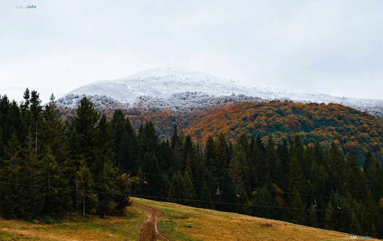 First snow on the peak of Pop Ivan mountain in the Carpathians: a snow-covered ridge above autumn forests and a cable car