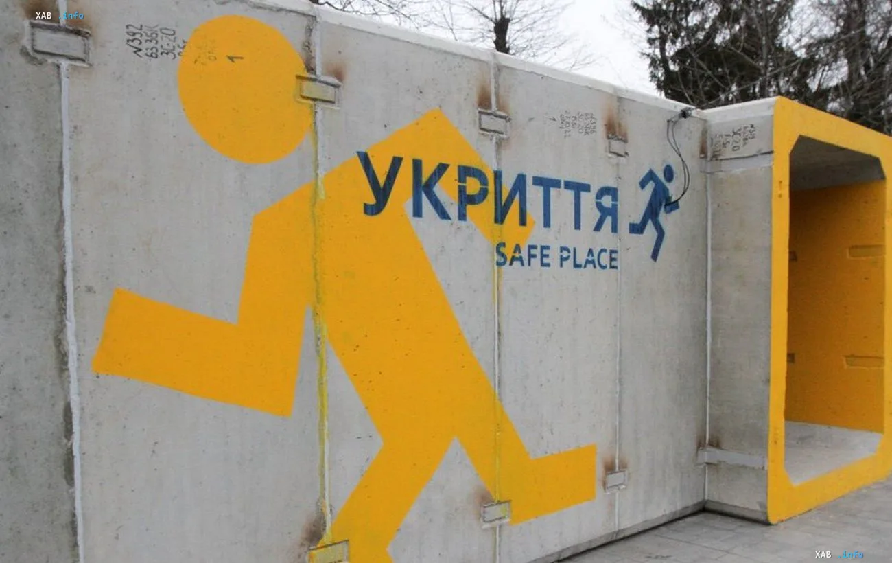 Mobile concrete shelter marked 'UKRYTTIA / SAFE PLACE' with a yellow running-figure pictogram, prepared by Kyiv city authorities instead of glass bus stops on Lukianivka