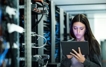 IT infrastructure specialist checking server status on a tablet in a data center server room