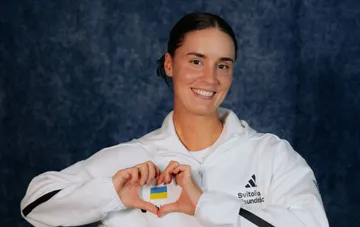 Ukrainische Tennisspielerin Kalynina in weißer Jacke mit ukrainischer Flagge formt mit den Händen ein Herz nach einem Comeback im Viertelfinale des Billie Jean King Cups