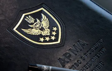 Emblem und die Aufschrift „ARMA“ auf einem schwarzen Ledergeschäftskoffer mit ukrainischen Symbolen, die das Thema der Verwaltung konfiszierter Vermögenswerte illustrieren