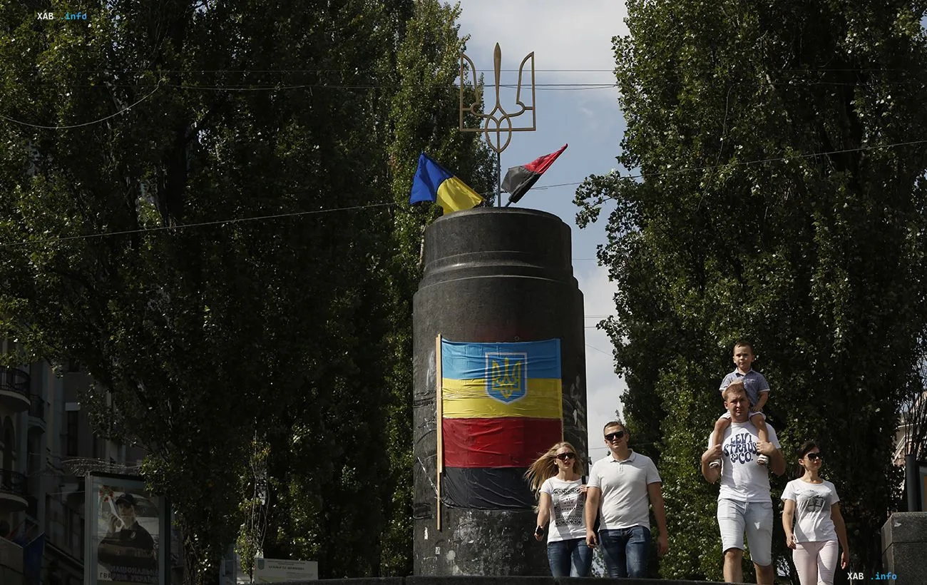 Ein Denkmal mit dem ukrainischen Wappen und Dreizack in der Kyjiver Innenstadt, im Hintergrund gehen Passanten vorbei