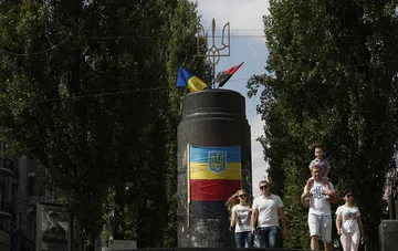 Ein Denkmal mit dem ukrainischen Wappen und Dreizack in der Kyjiver Innenstadt, im Hintergrund gehen Passanten vorbei