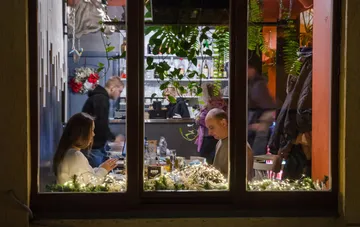 Ein ukrainisches Restaurant arbeitet auch während eines Blackouts weiter: Licht im Fenster, Gäste an den Tischen und Lichterketten vor dunkler Straße
