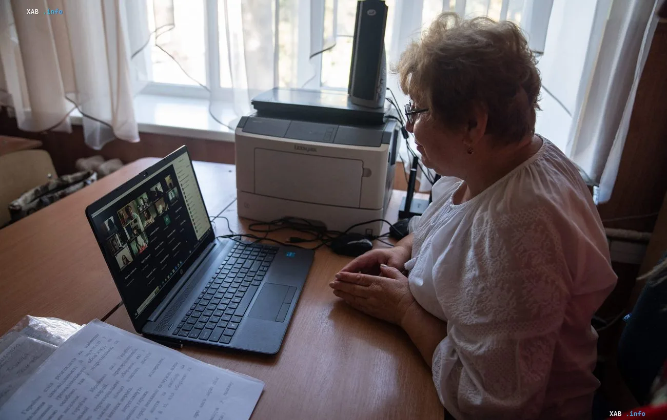 Учительница за ноутбуком с видеоконференцией на фоне новости о доплате педагогам прифронтовых территорий