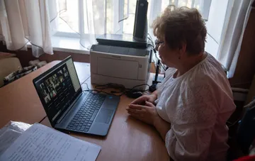 Учительница за ноутбуком с видеоконференцией на фоне новости о доплате педагогам прифронтовых территорий
