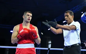 Павел Иллюша в красной боксёрской форме на ринге чемпионата Европы по боксу в Софии, судья останавливает раунд