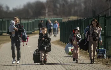 Families with children and luggage walk along a fence near the border, illustrating Ukraine's talks on relocating border crossings