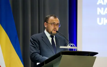 Украинский посол выступает за трибуной с микрофоном на фоне флага Украины, объясняя причины сокращения числа украинцев под временной защитой в Польше