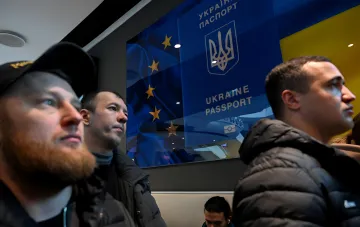 Мужчины стоят на фоне официального указателя с символикой Украины и Европейского Союза в помещении.