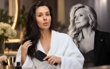 Masha Efrosinina in a white robe brushes her hair while recording a video message against the backdrop of Iryna Fedyshyn's portrait
