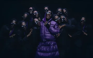 Група моделей та музикантів у фіолетових та чорних пуховиках Moncler зі співачкою в центрі