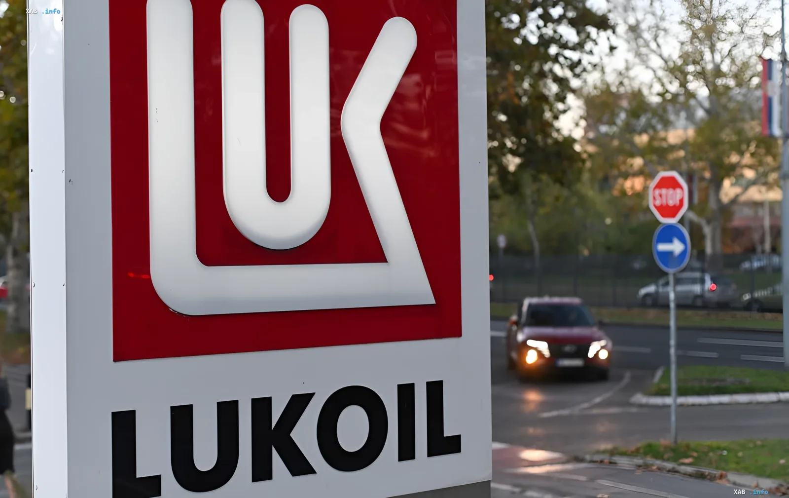 Nahaufnahme eines Lukoil-Tankstellenschilds mit rotem Logo und einer Straße im Hintergrund