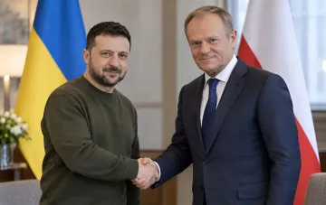 Владимир Зеленский и Дональд Туск жмут друг другу руки на фоне флагов Украины и Польши