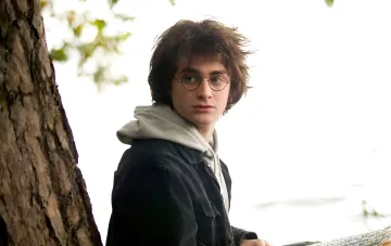 Harry Potter wearing glasses and with messy hair sitting by a tree