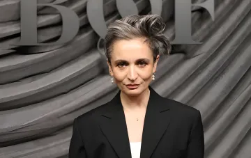 Veronica Leoni with short gray hair and pearl earrings wearing a black blazer at an event