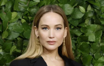 Schauspielerin Jennifer Lawrence mit blonden Haaren und schwarzem Outfit vor grünem Laub