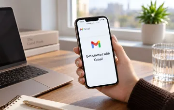 Smartphone in a user's hand displaying the Gmail app on screen against a laptop background