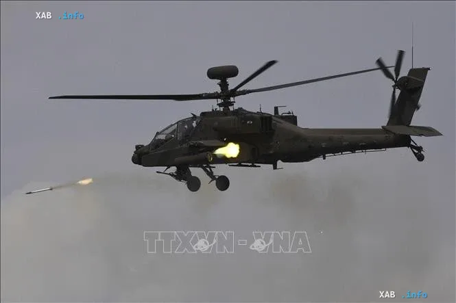 Военный ударный вертолет AH-64 Apache в полете запускает ракету в ходе учений