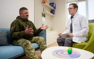 A military serviceman in camouflage communicates with a doctor in a bright consultation room of a support center