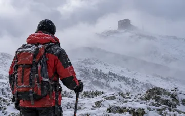 Mountaineer in a red jacket looking at a snow-covered mountain peak in the fog