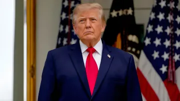 Donald Trump in a dark blue suit with a red tie against the background of American flags