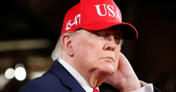 Дональд Трамп в красной кепке с надписью USA на фоне политического мероприятия