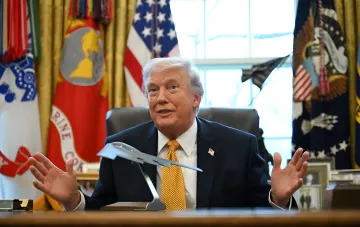Donald Trump sitting at a desk in the Oval Office against the backdrop of the American flag