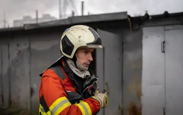 Пожежний у захисному шоломі та спецодязі на тлі руйнувань у місті після атаки безпілотників