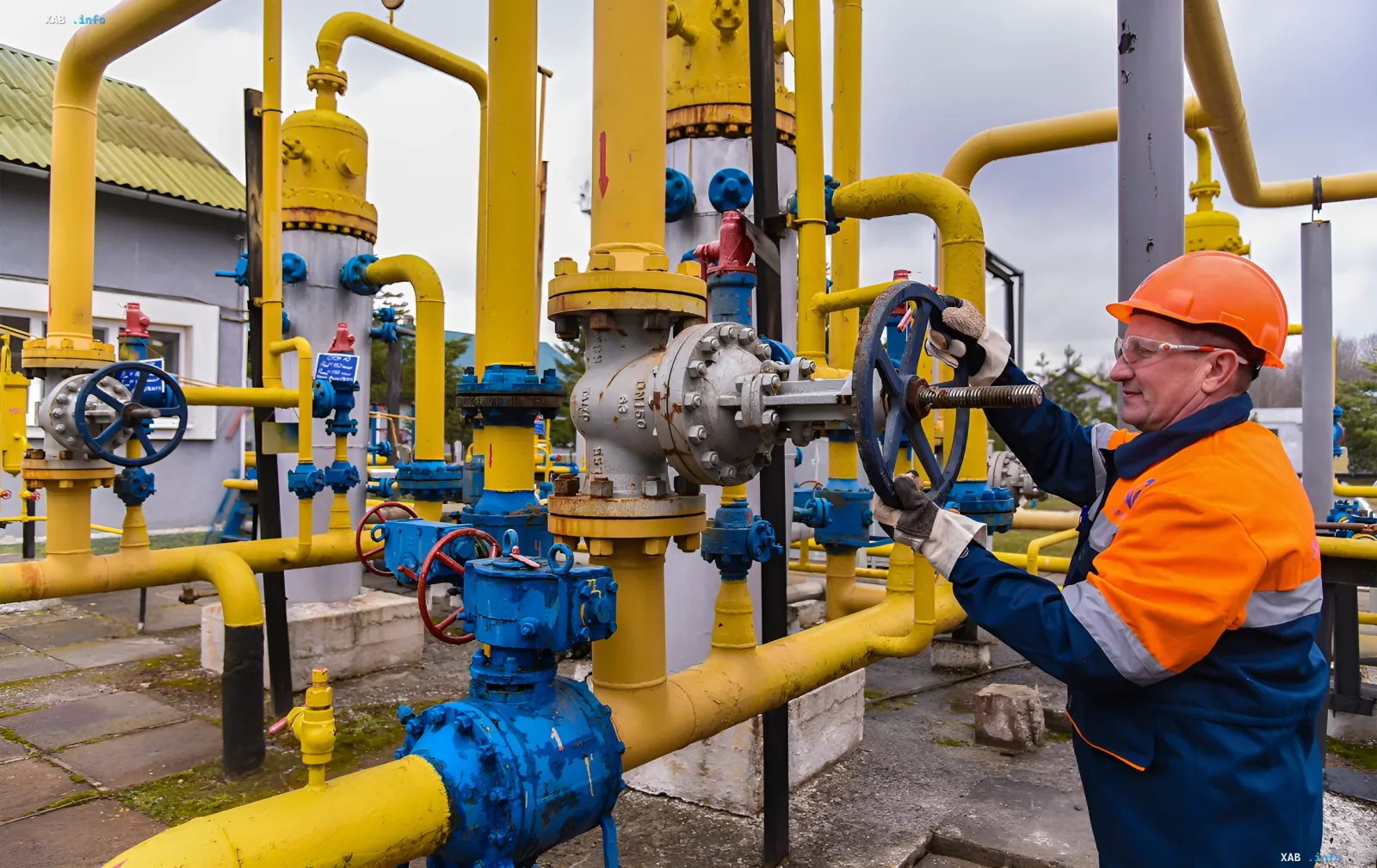 Работник в каске и защитных очках поворачивает вентиль на газовом объекте с желтыми трубами