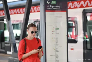 Frau in Sonnenbrille schaut auf ihr Smartphone an einer Moskauer U-Bahn-Station vor dem Hintergrund der Linienkarte D4