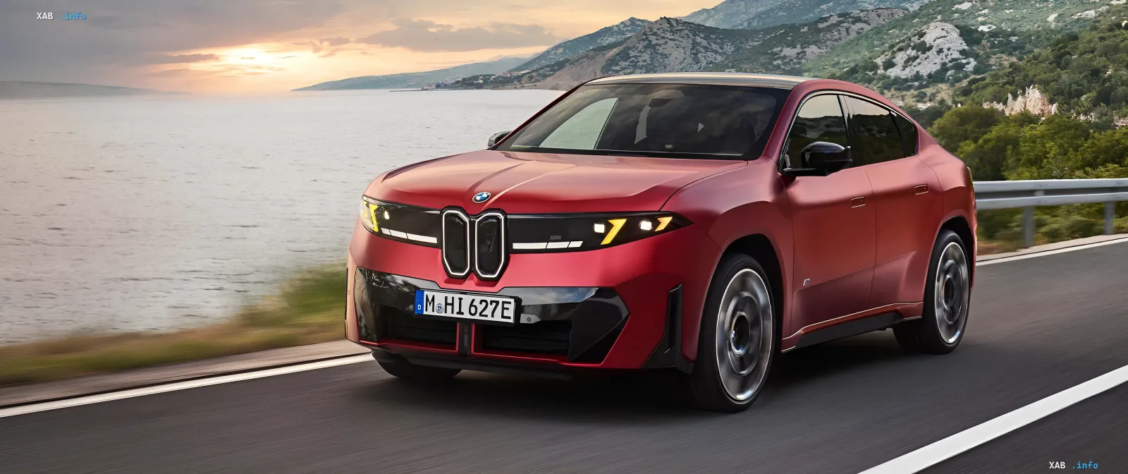 Красный электромобиль BMW движется по прибрежной дороге на фоне заката
