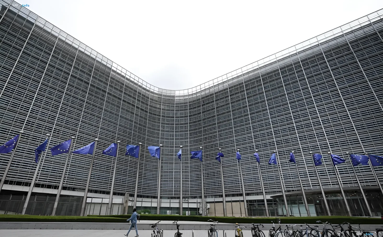 The European Commission building in Brussels featuring EU flags lined up beneath an overcast sky.