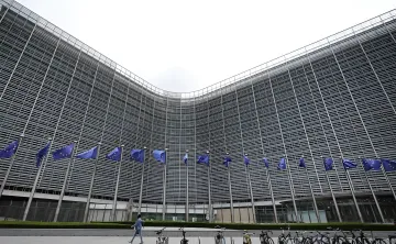 The European Commission building in Brussels featuring EU flags lined up beneath an overcast sky.