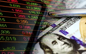 Stock market charts on a monitor and a stack of American dollars with a 100-dollar bill
