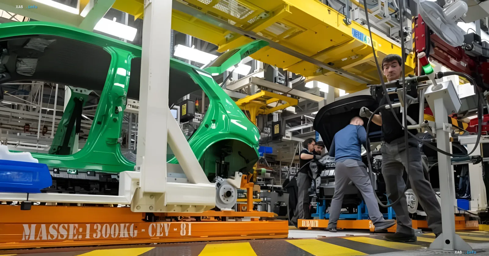 Workers assemble cars at a modern European automotive plant beneath yellow conveyor structures